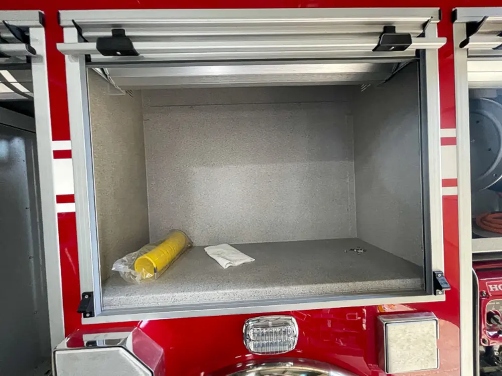 Exterior view of small fire truck showing cab, body compartments, and wheel/tire area.